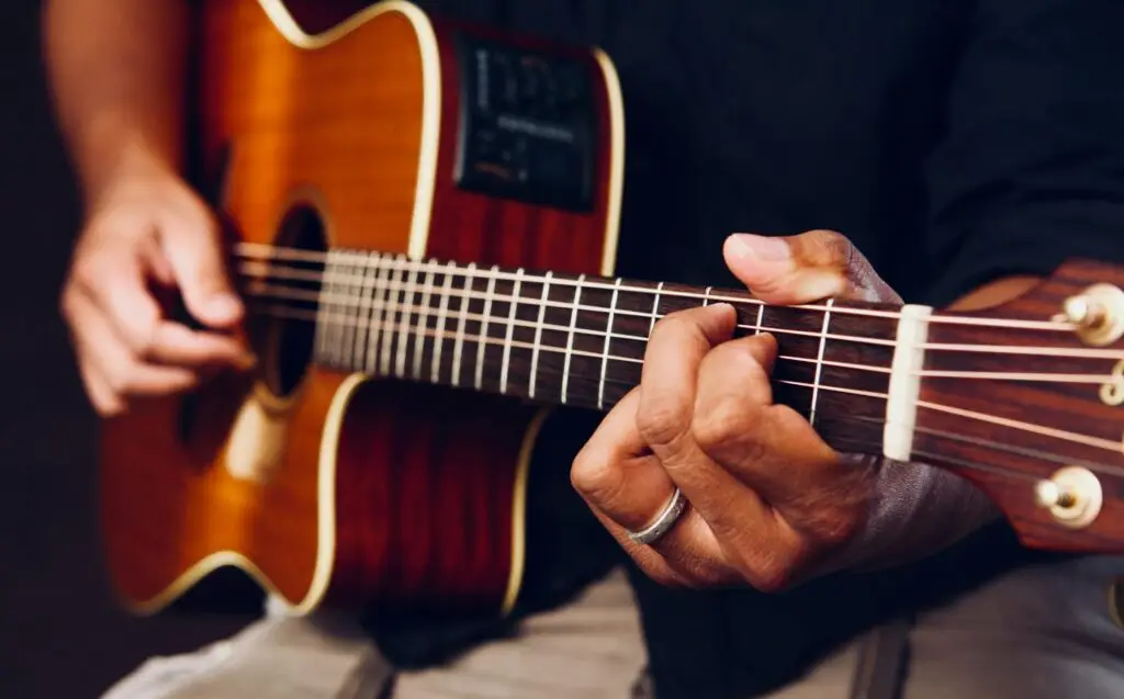 Hands playing an acoustic guitar, showcasing chords and frets up close.
